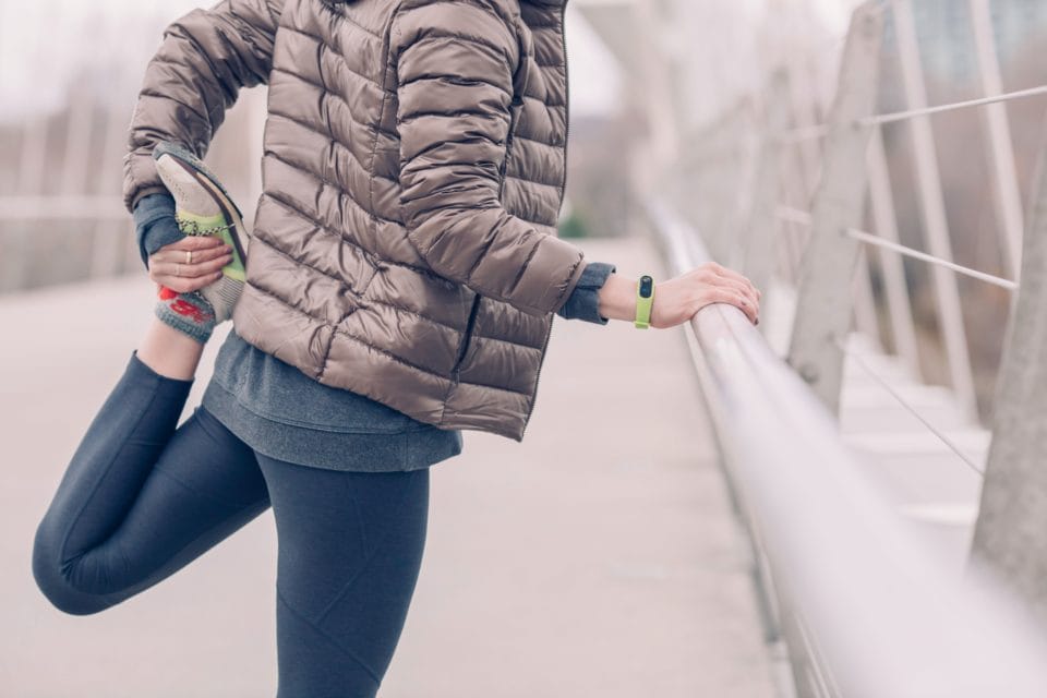 woman doing a quad stretch outside on a bridge