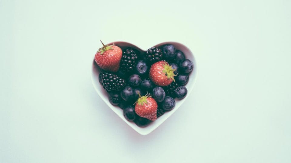 heart bowl with blueberries, raspberries, and black berries in itwith green background